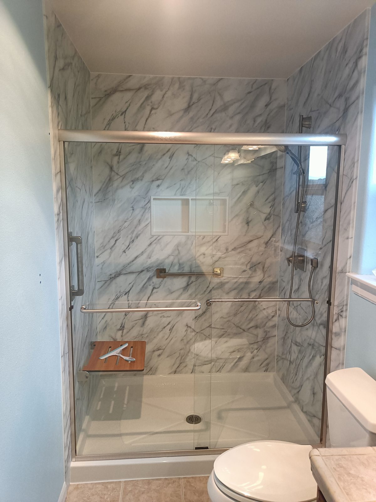 Accessible walk-in shower with teak fold-down seat, grab bars and glass doors