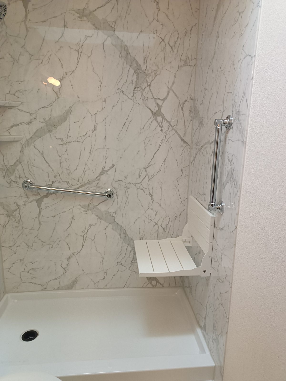 Fold-down shower seat and grab bars in a marble-look shower — accessible bathroom remodel