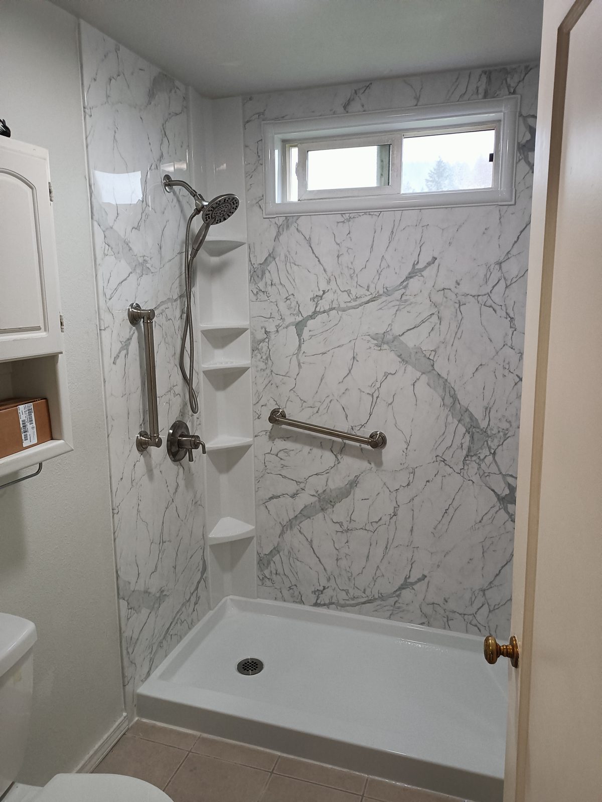 Bright marble-look shower with corner shelves, grab bars and low-threshold pan
