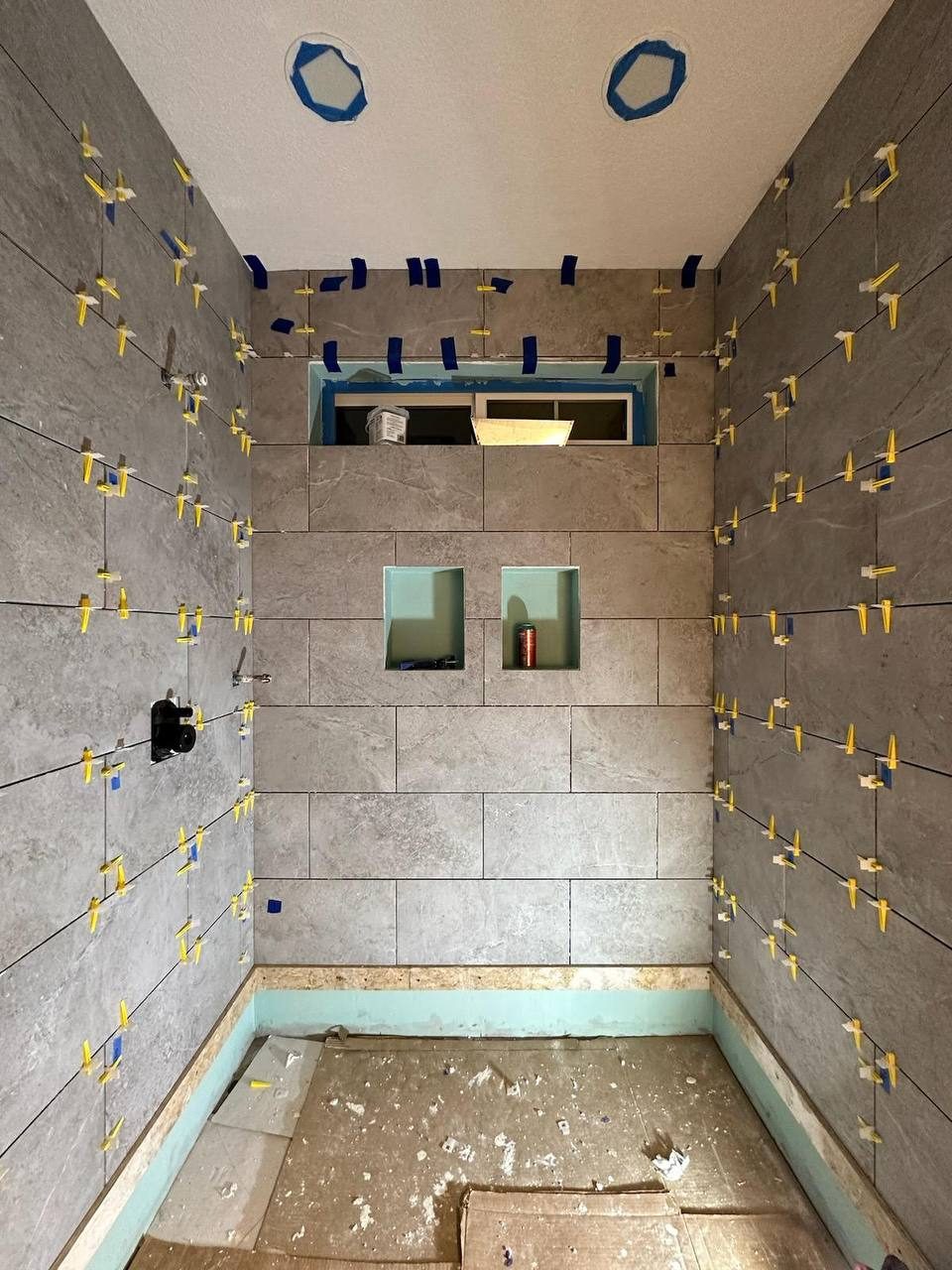 Large-format shower tile being set with leveling spacers — floor-to-ceiling custom tile work in progress